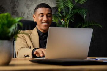 Smiling African American businessman working with laptop in cozy office with plants