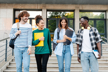 Happy students walking together on university campus, chatting and laughing outdoors after classes - obrazy, fototapety, plakaty