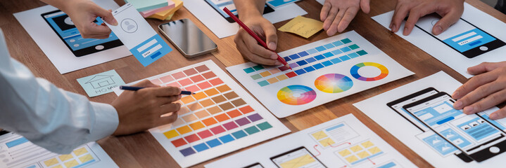 Panorama shot of front-end developer team brainstorming UI and UX designs for mobile app on paper...