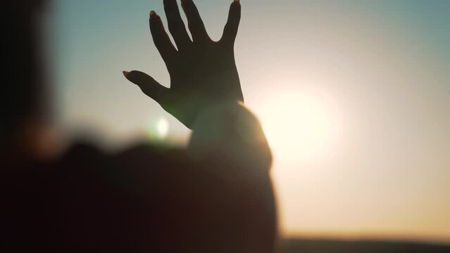 Happy girl pulls her hand towards the sunlight. Silhouette of man in natural park. Girl stretches her hand to the sky. Sun rays through fingers. Woman stretches her hand to sky in nature park