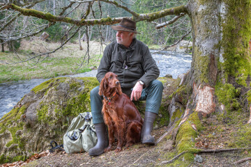 The hiker and his Irish Setter have completed a strenuous hike and are taking a break by the...