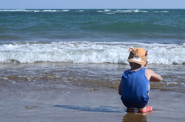 A little boy sits on the seashore plays with sand and breathes the sea air