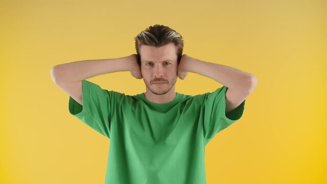 A person standing in front of a yellow background covers his mouth with his hands, then his ears, and then his eyes. A man stands in front of the camera and makes gestures of three monkeys.