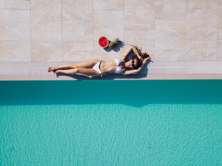 Beautiful sexy woman model in white bikini lies near swimming pool, posing and tanned on summer...
