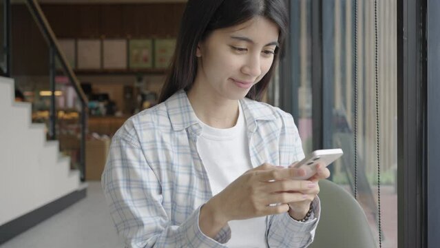Asian women using smartphone to send text message, read message, playing social media in coffee shop. wireless technology 5G.