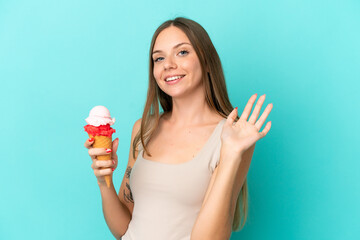 Young Lithuanian woman with cornet ice cream isolated on blue background saluting with hand with happy expression