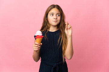 Child with a cornet ice cream over isolated pink background with fingers crossing and wishing the...