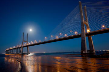 The Vasco da Gama Bridge in Lisbon, Portugal at night with moon. Cable-stayed bridge. Tagus river. Horizontal shot. Long exposure.