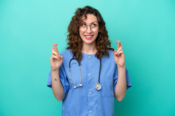 Young nurse caucasian woman isolated on blue background with fingers crossing