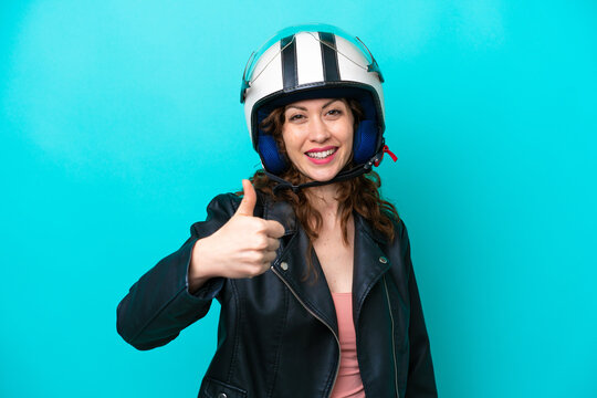 Young caucasian woman with a motorcycle helmet isolated on blue background with thumbs up because something good has happened