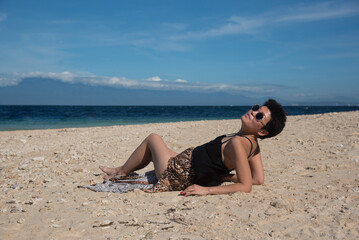 Asian girl lying at the beach in summer vacation. Stylish pretty woman with short black hair and leopart skirt. Copy space and blue sky on the background. Beauty lady with sunglasses.