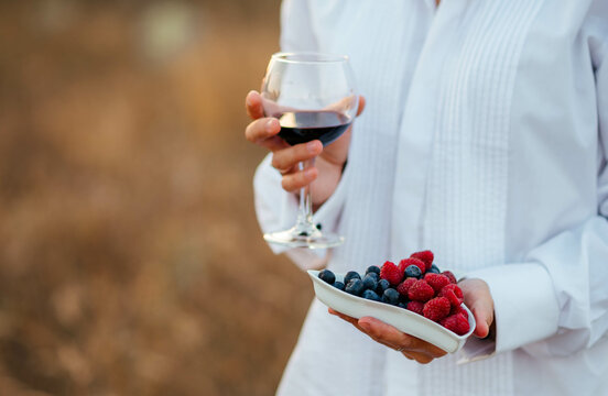 Girl in a white shirt with a glass of red wine and a plate of blueberries and raspberries. 