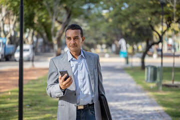 Young latin man in suit walking with mobile phone in hand.