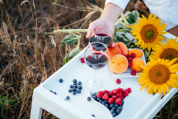 Romantic picnic in nature. Two glasses of red wine, berries and fruits on a white table with a bouquet of sunflowers. 