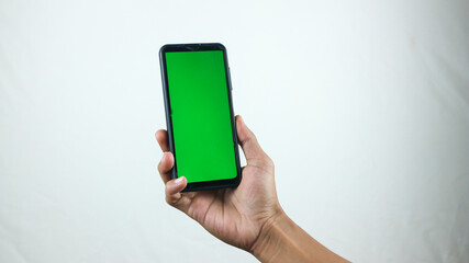 Asian man holding big smartphone with white, red, green, blue blank screen in hand, showing close to camera and pointing at device. Gadget with empty free space for mock up, banner