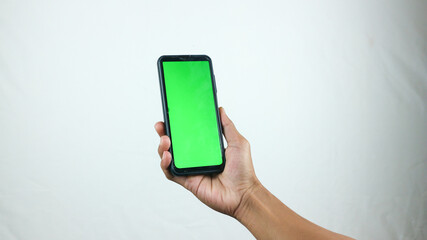 Asian man holding big smartphone with white, red, green, blue blank screen in hand, showing close to camera and pointing at device. Gadget with empty free space for mock up, banner