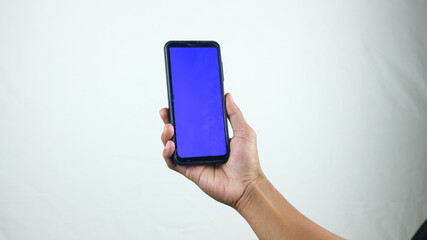 Asian man holding big smartphone with white, red, green, blue blank screen in hand, showing close to camera and pointing at device. Gadget with empty free space for mock up, banner