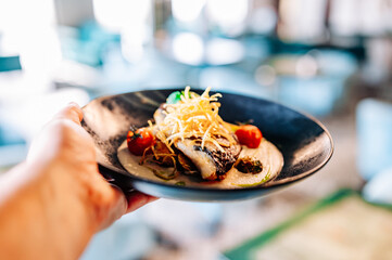 man hand hold Fried fillet dorado fish with tomatoes, lemon and sauce on plate