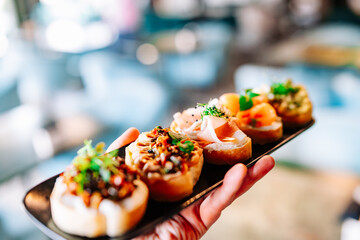 man hand hold various bruschettas with toppings on black plate
