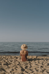 Pretty woman sitting on beach sand and watching at sea and sky. Minimal summer vacation concept....
