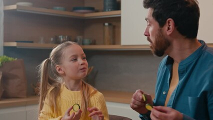 Caucasian father with little daughter at home kitchen cooking eating together child girl kid feed dad with cucumber slice daddy joking pretend feeding baby deceive cheat fooling around happy family - Powered by Adobe