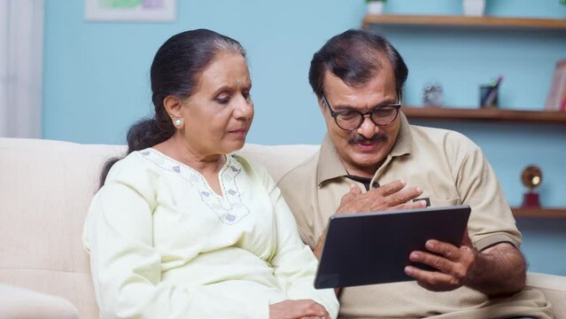 Indian senior couple talking with doctor on video call using digital tablet at home - concept of online consultation, medicare and home health care