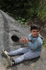 
the boy dug a hole in the sand, the child smiles and looks away