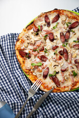 Pizza with mini sausages, bacon, meat, mushrooms and cheese. Thin homemade Italian pizza. Food background. Plate top view