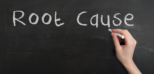 Fototapeta premium A woman's hand write text Root cause with chalk on chalkboard