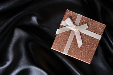 Pink gift box with bow background with black silk fabric.