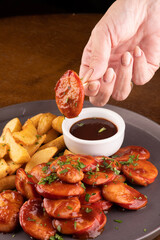 woman's hand picking a sausage from a portion of bock sausages with country fries and barbecue sauce and curry pint of pale ale at a round table