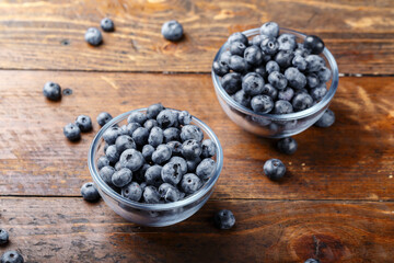 Freshly picked blueberries in a glass bowl on a wooden background. Healthy food and nutrition concept.