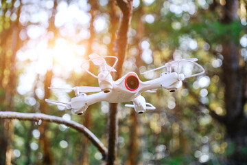 Flying quadcopter in forest against background bright sun.