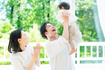 新緑の前で赤ちゃんを高い高いする両親