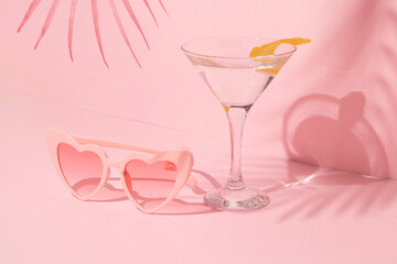 Summer creative layout with  heart sunglasses, martini coctail glass and palm leaf on pastel pink background. 80s or 90s retro aesthetic idea. Minimal summer fashion idea.