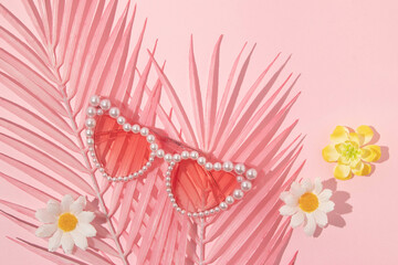 Summer creative layout with pink palm leaves, heart sunglasses and flowers on pastel pink...