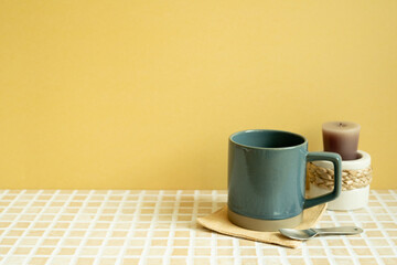 Navy mug cup and candle on check tile table. yellow wall background