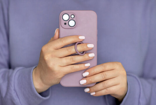 Close-up woman with white wanicure hold in hand and use mobile cell phone in puple case with ring. No face.