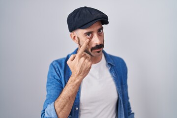 Hispanic man with beard standing over isolated background pointing to the eye watching you gesture, suspicious expression