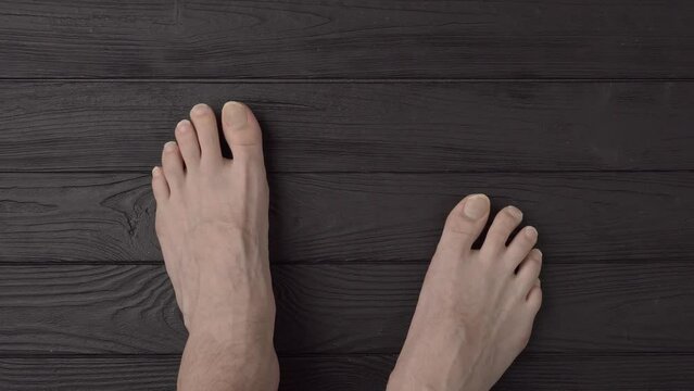 Male feet with extremely long and terribly untrimmed nails on a black wooden background or floor. Close up, top view, point of view