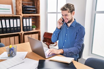 Young man business worker using laptop talking on smartphone at office