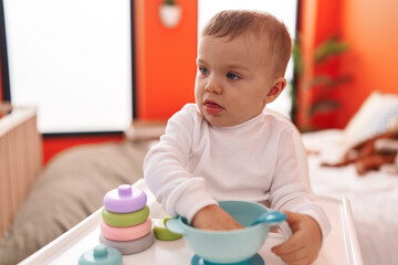 Adorable blond toddler sitting on highchair playing at bedroom