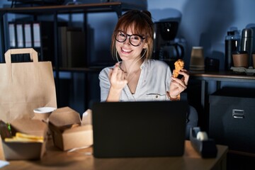 Young beautiful woman working using computer laptop and eating delivery food beckoning come here gesture with hand inviting welcoming happy and smiling