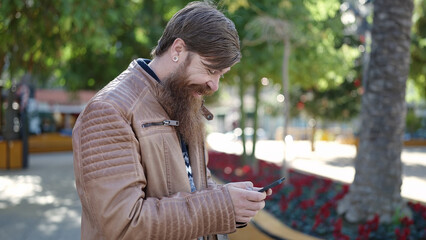 Young redhead man smiling confident using smartphone at park