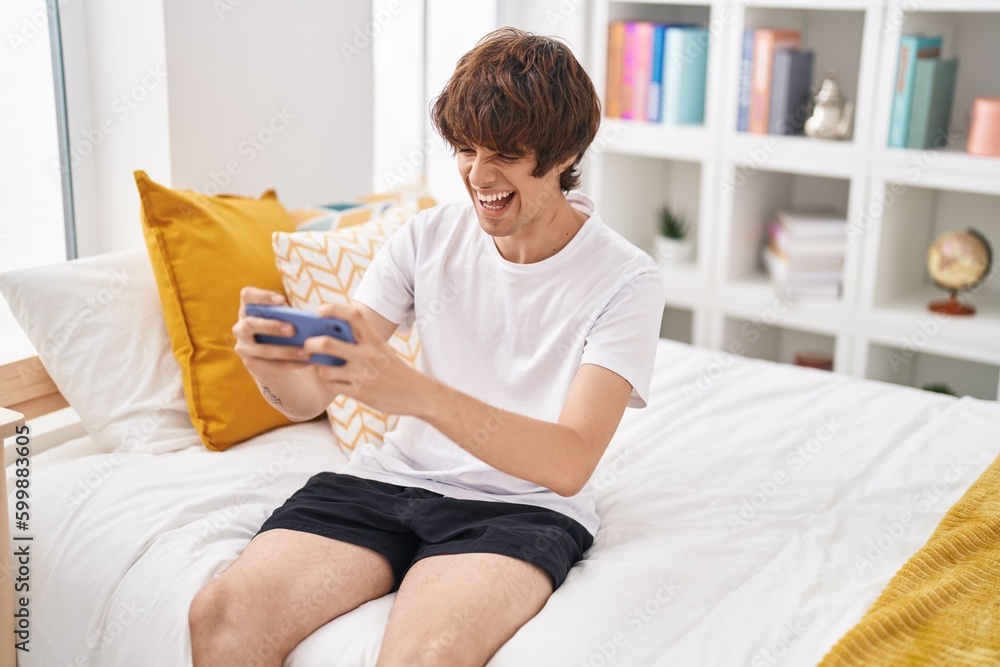 Sticker Young blond man playing video game sitting on sofa at bedroom