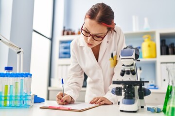 Young caucasian woman scientist writing report working at laboratory
