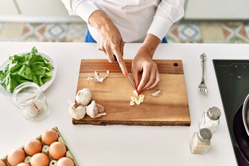 Young blonde woman cutting garlic at kitchen