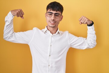 Fototapeta premium Young hispanic man standing over yellow background showing arms muscles smiling proud. fitness concept.