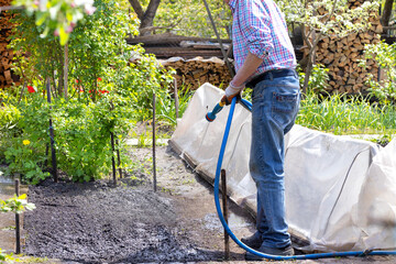 A gardener is watering the beds in the garden with a garden sprayer in the garden yard on a bright spring day.