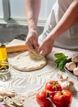 hands of the cook in the kitchen sprinkle the dough with flour. dough for pizza.